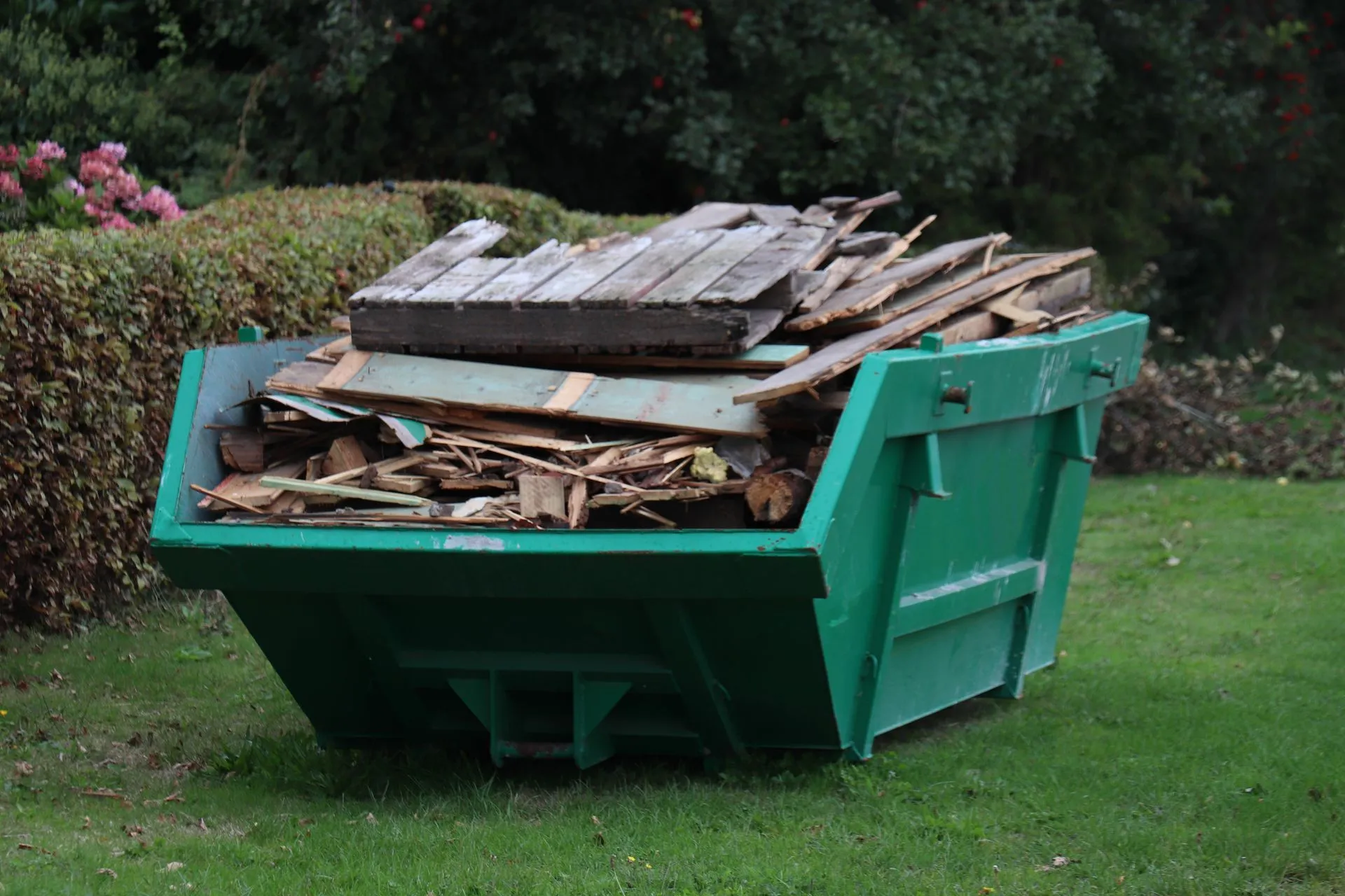 A green dumpster filled with wood is sitting on top of a lush green lawn.